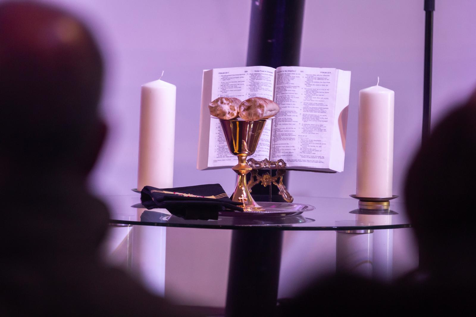 Communion bread, cup and open Bible on a glass table