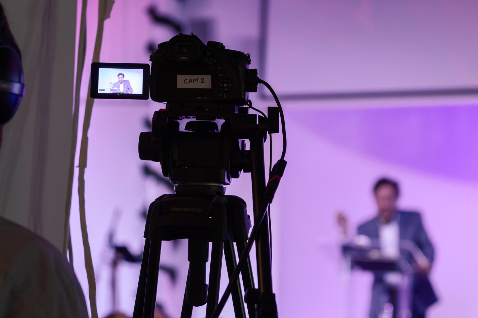 CAM 2 broadcast tripod with Pastor Chris preaching in the background