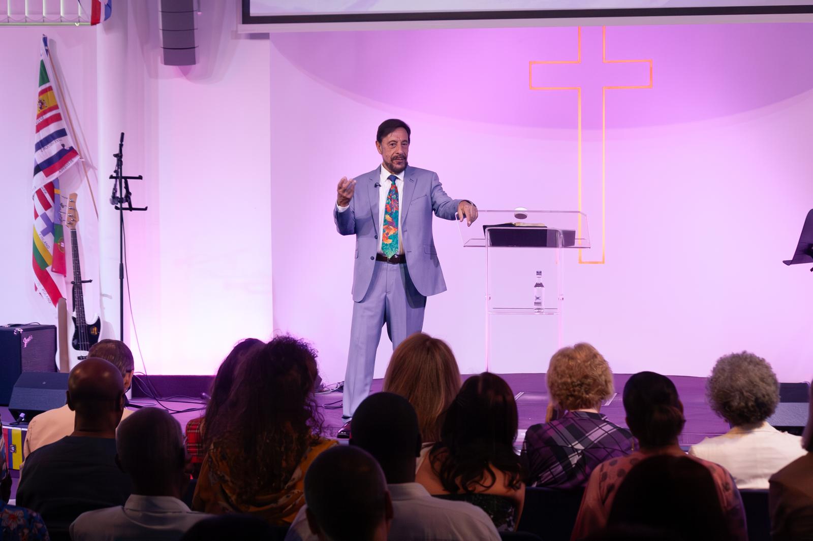 Pastor Chris preaching to the congregation in a light suit