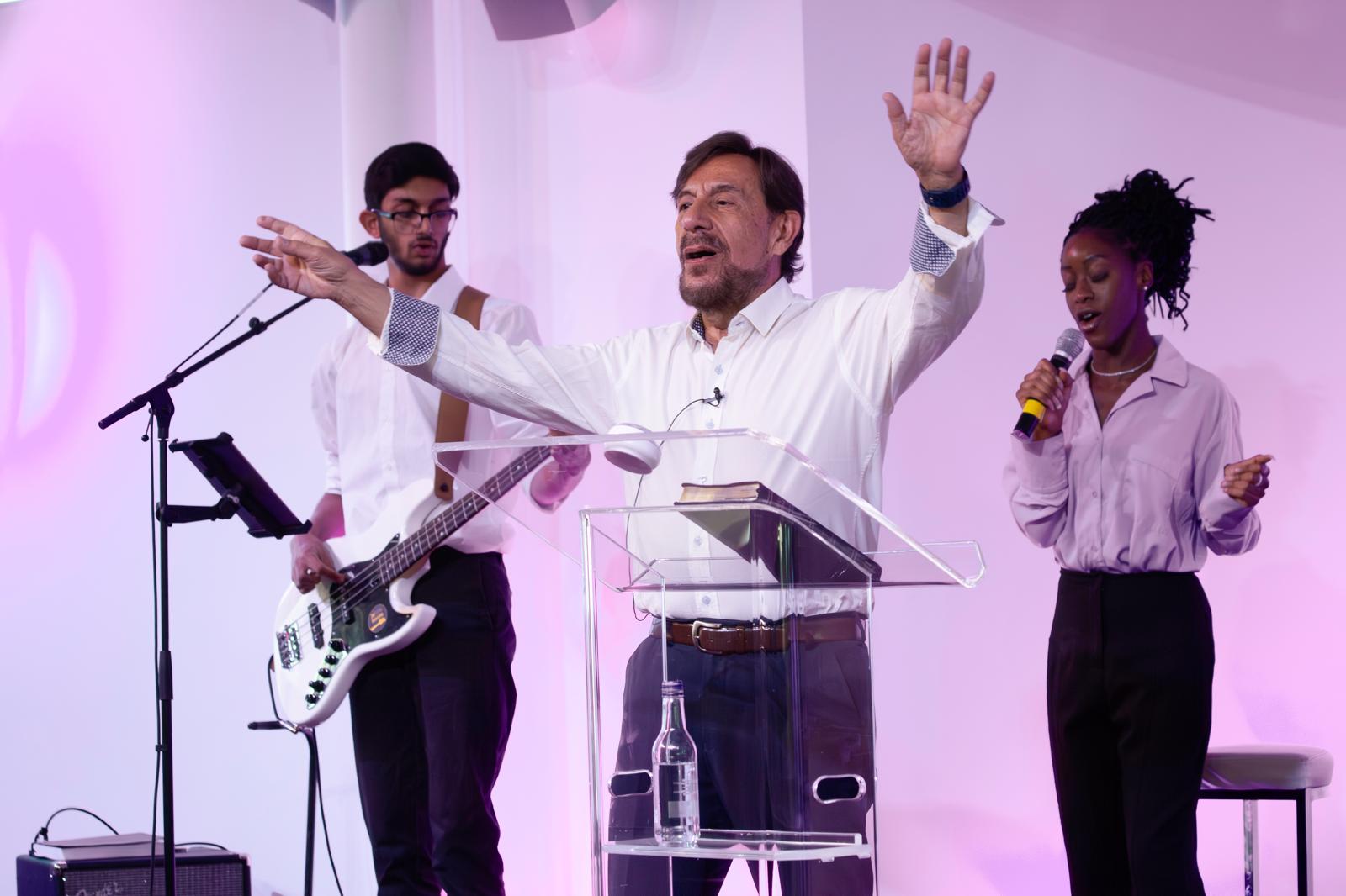 Pastor Chris worshipping on stage with hands raised, alongside the worship band