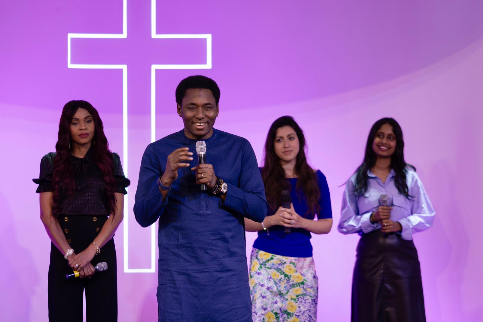 Valentine Agwu speaking with a microphone, three women on stage behind him
