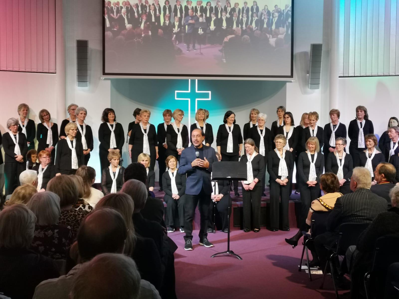 A visiting choir in white scarves performing on stage at Cornerstone with their director
