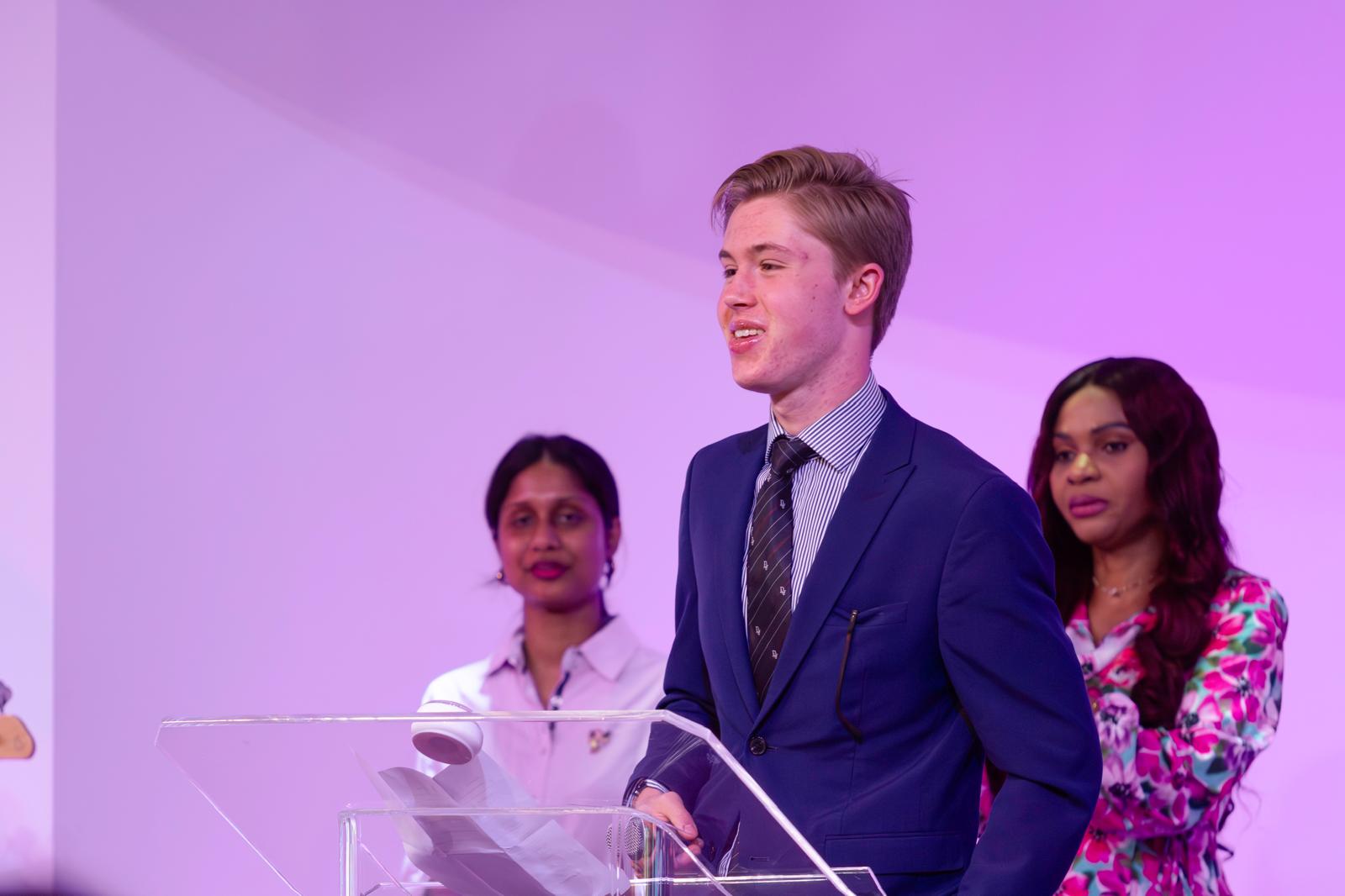 A young man sharing his testimony at the lectern, two women behind him
