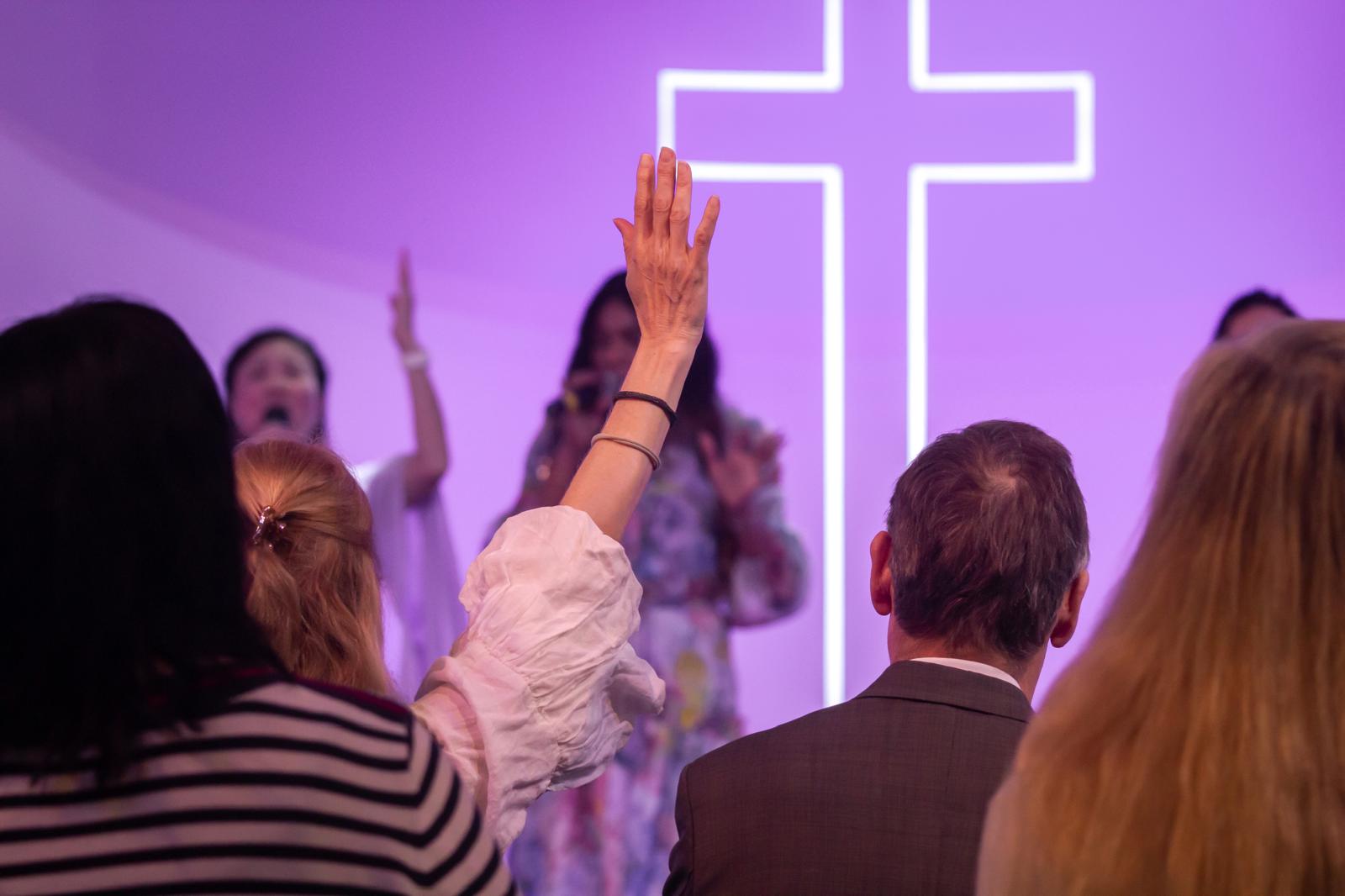 A single hand raised in worship before the neon cross
