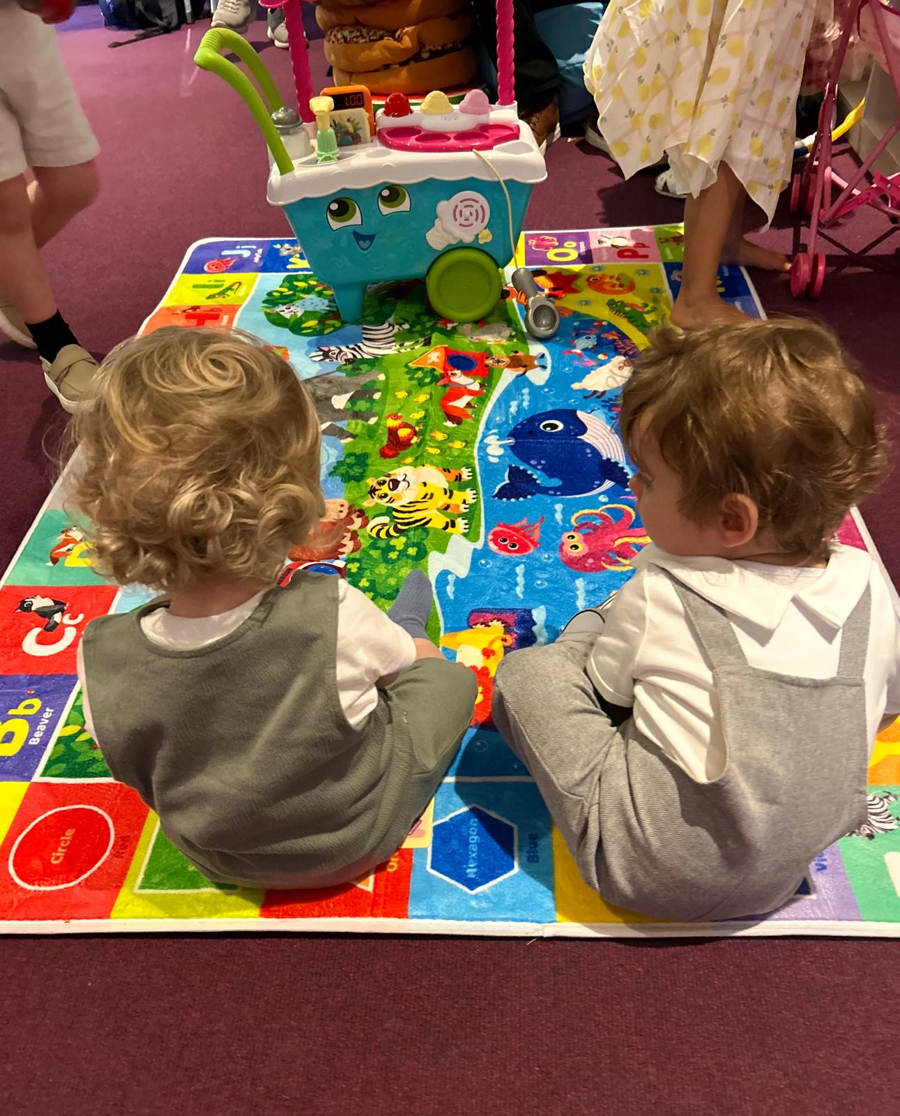 Two toddlers playing together on a colourful alphabet mat in the Little Lambs creche at Cornerstone The Church