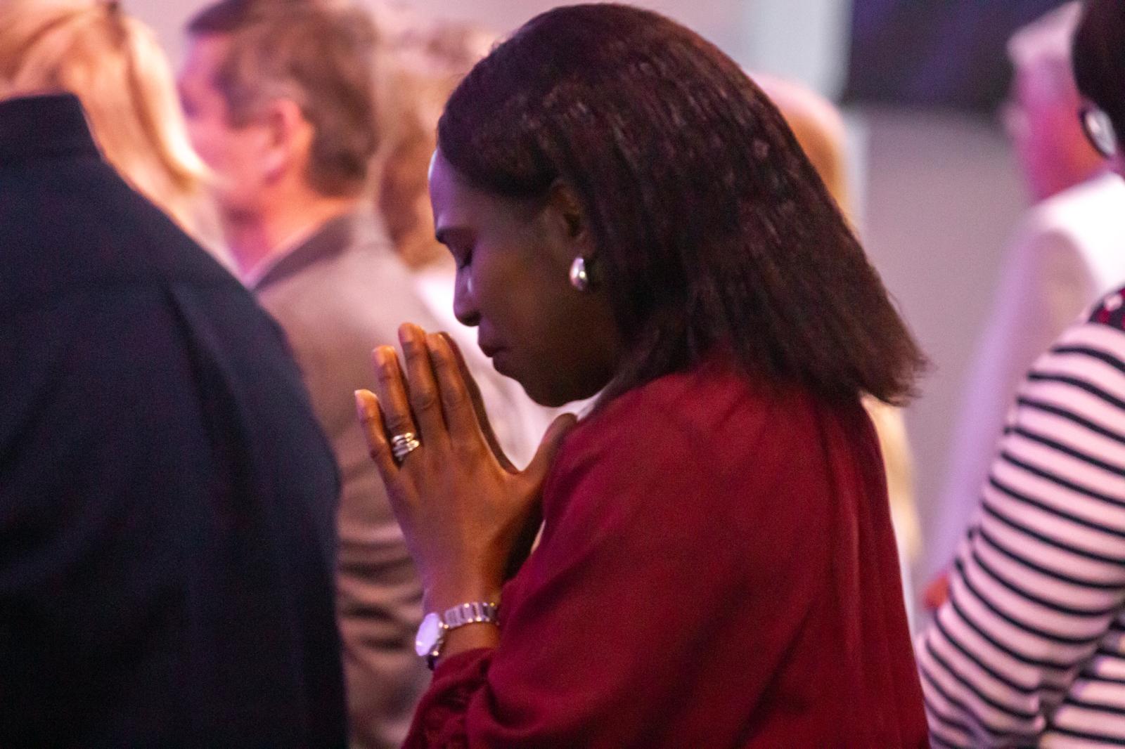 A woman in red praying, hands clasped, eyes closed
