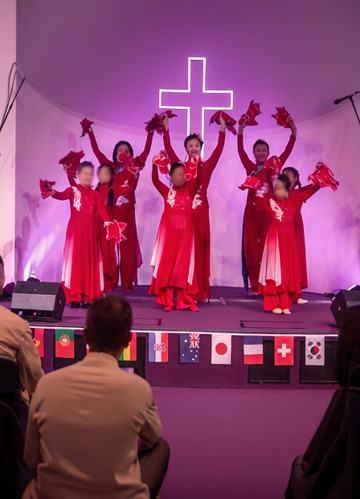 Cornerstone dancers in red Chinese dresses with red fans, performing on stage before the cross